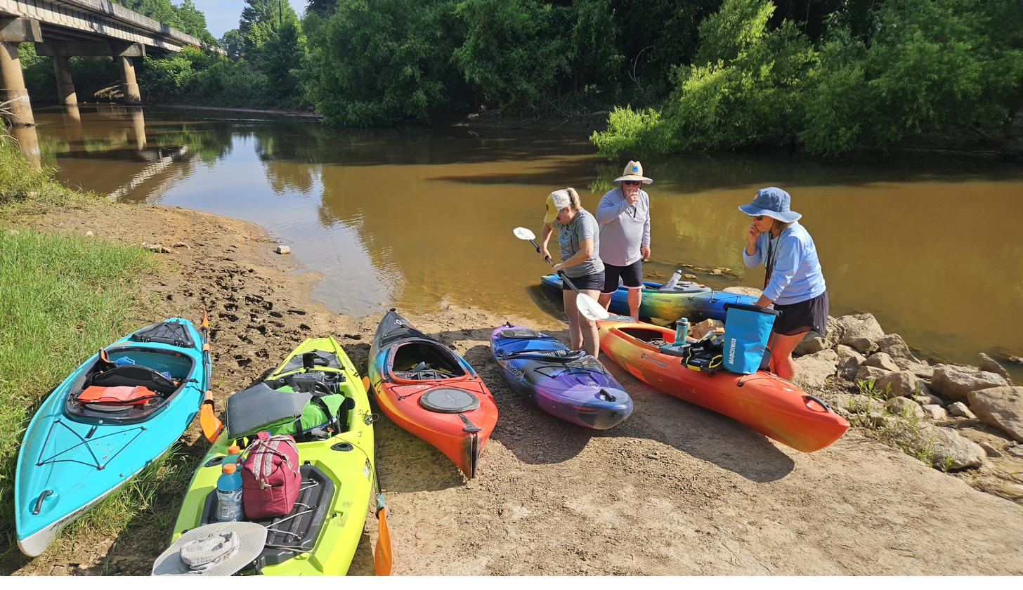 A group of guests with kayaks on the shore near Cypress Landing